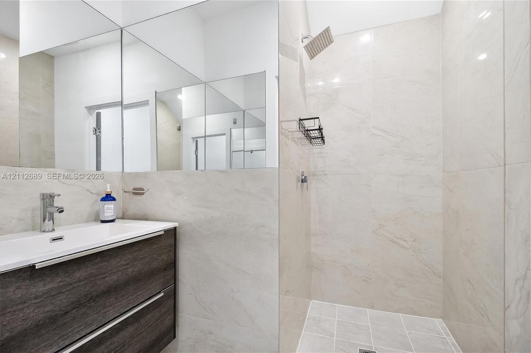 Modern floating vanity with a dark wood-finish exterior, integrated rectangular sink, wall-spanning mirror, and a walk-in shower featuring large-format wall tile and a rainfall showerhead