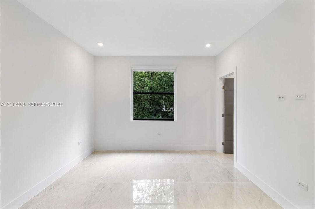 Interior space featuring large-format polished tile flooring, recessed lighting, neutral wall paint, and a single window with exterior greenery
