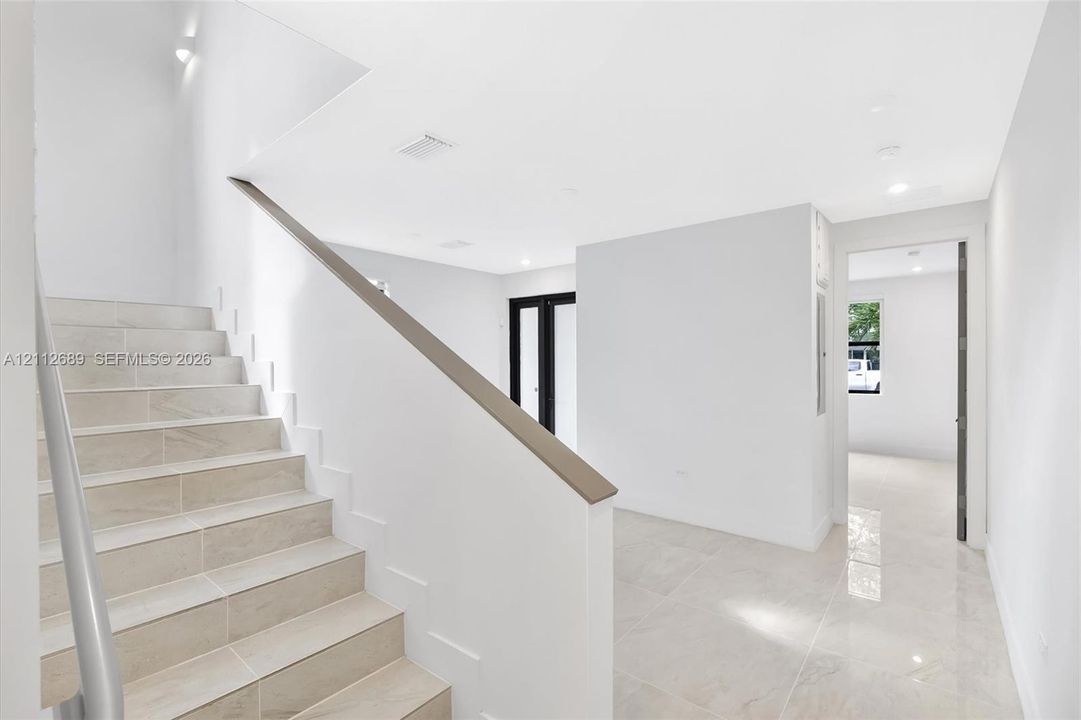 Staircase with tile-finished treads and a sleek handrail, polished tile flooring, and recessed ceiling lighting
