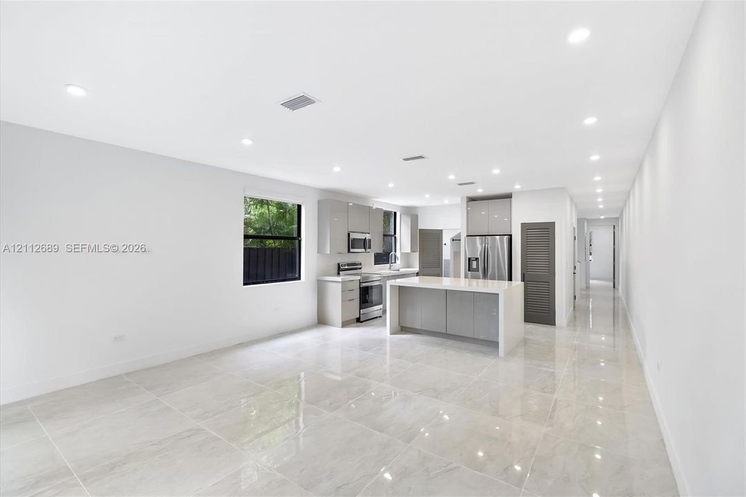 Kitchen featuring high-gloss cabinetry, stone-finish countertops, stainless steel appliances, a central island, and large-format porcelain tile flooring