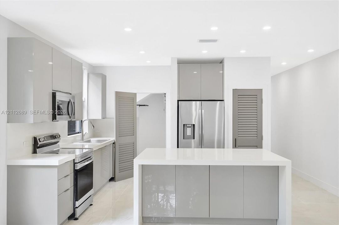Contemporary kitchen featuring high-gloss cabinetry, a central island with a solid-surface countertop, stainless steel appliances, recessed ceiling lighting, and large-format tile flooring