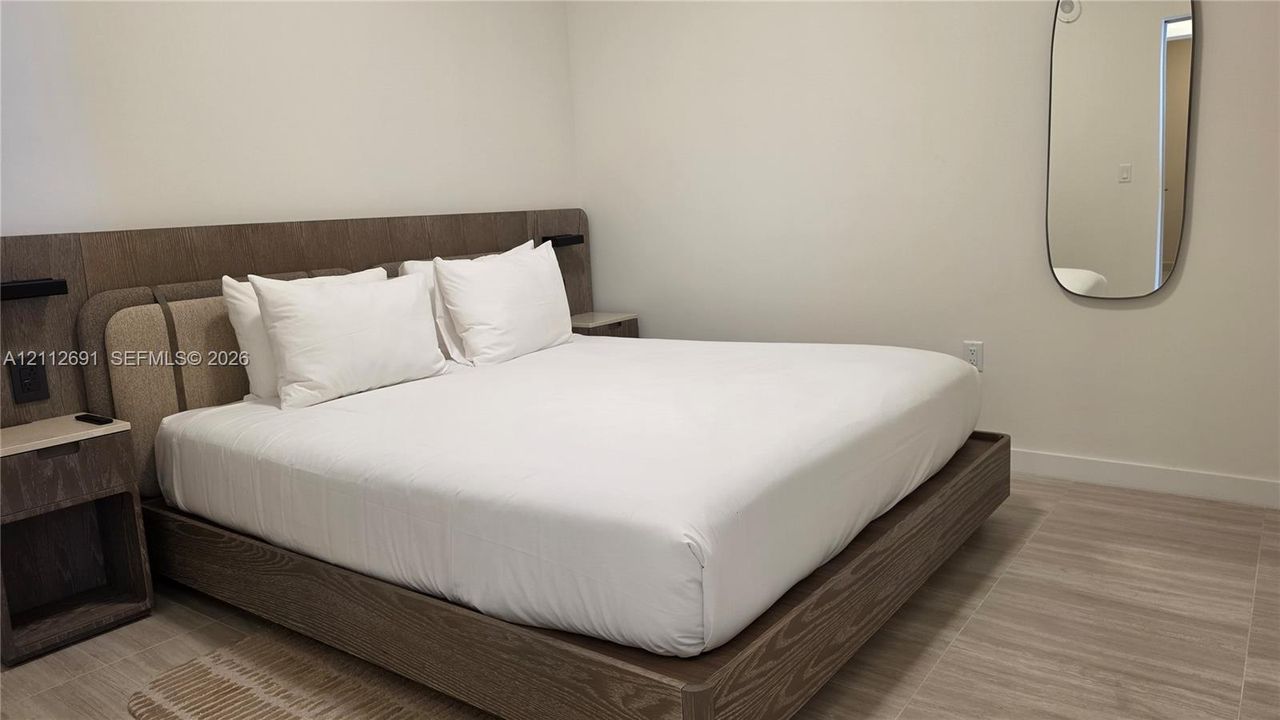 Built-in wood-finish platform bed frame with integrated side tables, wood-finish flooring, and wall-mounted oval mirror