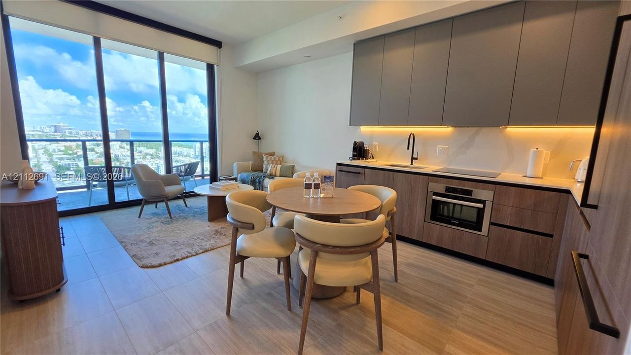 Modern kitchen featuring flat-panel wood-finish cabinetry, solid-surface countertops, integrated under-cabinet lighting, and floor-to-ceiling glass sliding doors