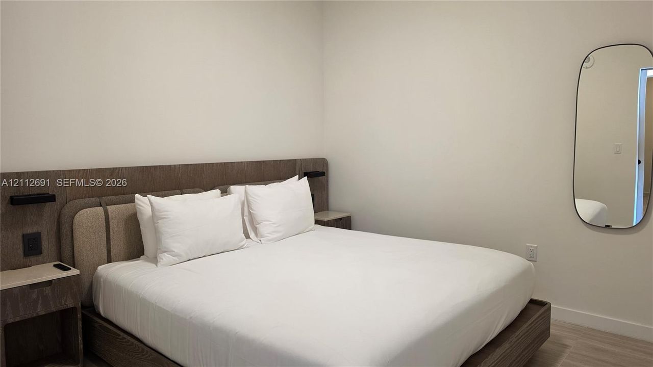 Integrated wood-finish headboard with built-in side tables, low-profile bed platform, and oval wall-mounted mirror