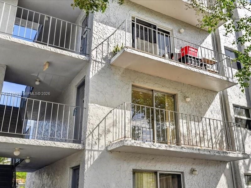 Multi-story exterior featuring a textured stucco facade, stacked private balconies with metal railings, and sliding glass door entries