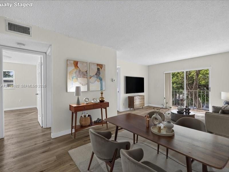 Open-concept interior featuring wood-finish flooring, sliding glass doors to a balcony, and white-painted walls