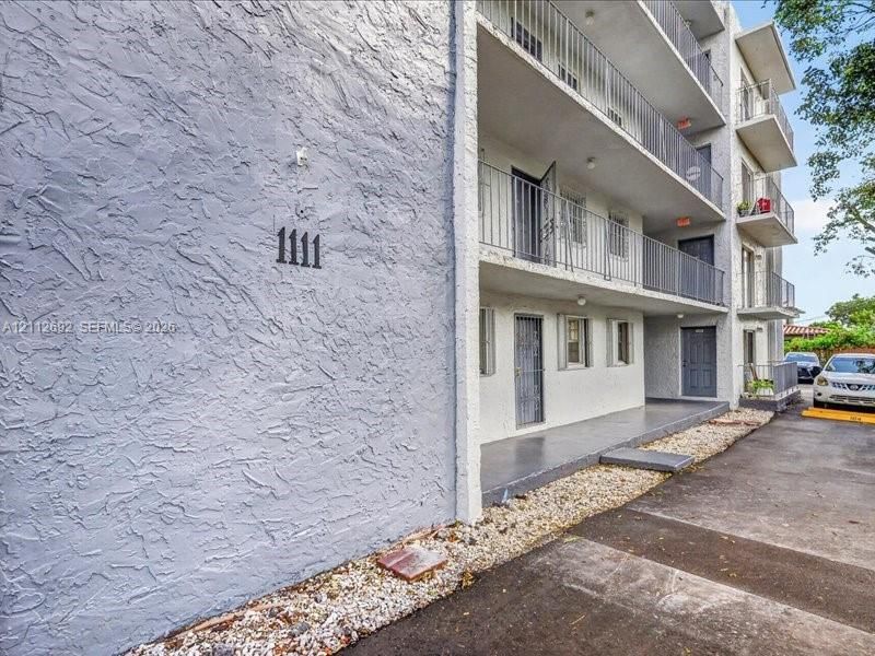 Multi-level building exterior featuring textured stucco siding, stacked balconies with metal railings, and a gravel border