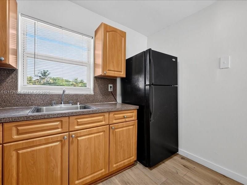 Kitchen featuring natural finish wood cabinetry, stone-textured countertop, stainless steel sink with a chrome faucet, black refrigerator, and wood-finish flooring