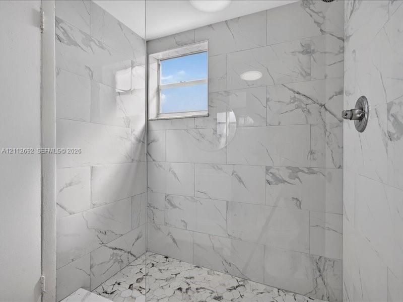 Walk-in shower featuring large-format porcelain wall tile, hexagonal floor tile, a recessed window, and a wall-mounted faucet fixture