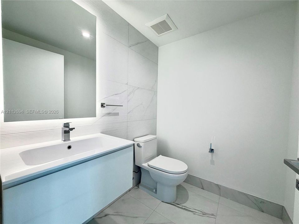Floating vanity with a rectangular sink, integrated LED mirror, large-format stone-patterned wall tile, and polished metal faucet
