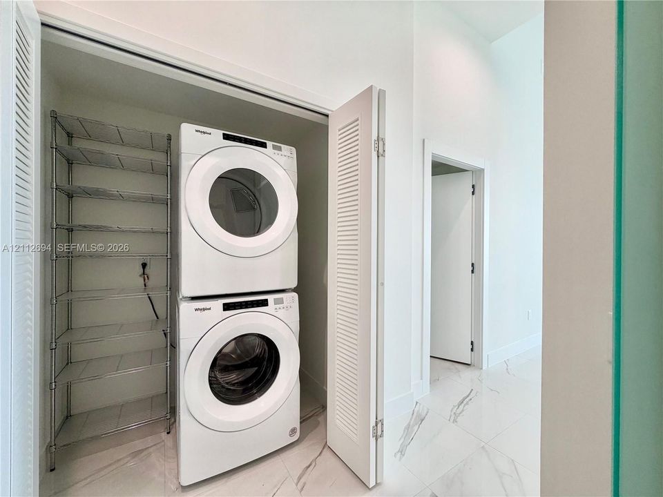 Laundry closet featuring louvered bifold doors, stone-finish tile flooring, and integrated metal shelving