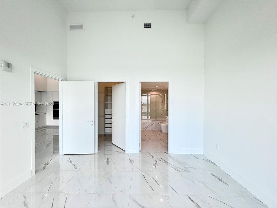 High-ceiling interior featuring polished, large-format stone-patterned tile flooring, minimalist white solid-core doors, and built-in closet shelving