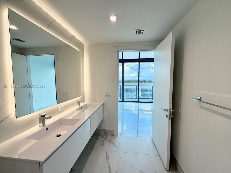Modern floating vanity with dual integrated sinks, quartz countertop, large backlit mirror, and floor-to-ceiling stone-finish tile flooring