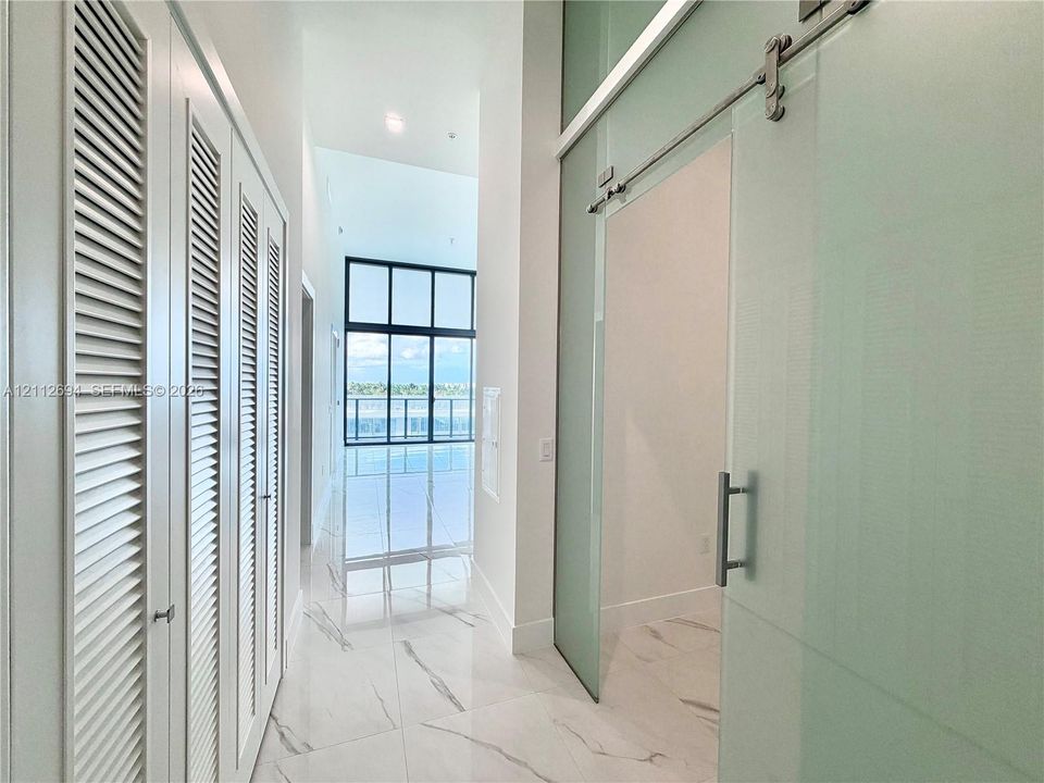 Hallway featuring large-format stone-finish flooring, floor-to-ceiling louvered cabinetry, and a sliding glass door with a polished metal track system