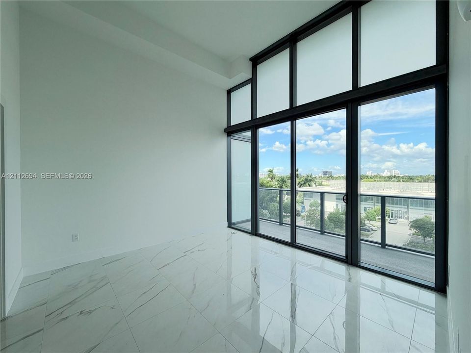 Floor-to-ceiling windows with black metal framing, polished white tile flooring, and integrated glass balcony door