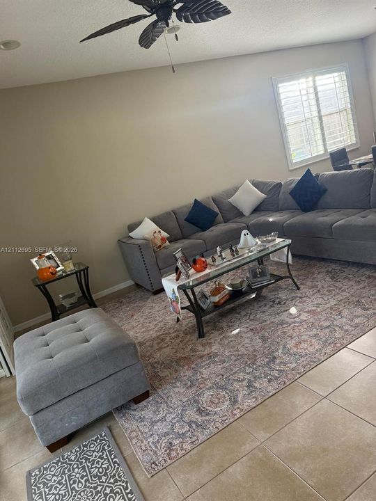 Neutral wall palette featuring large-format tile flooring, plantation shutters, and a ceiling-mounted fan with integrated lighting