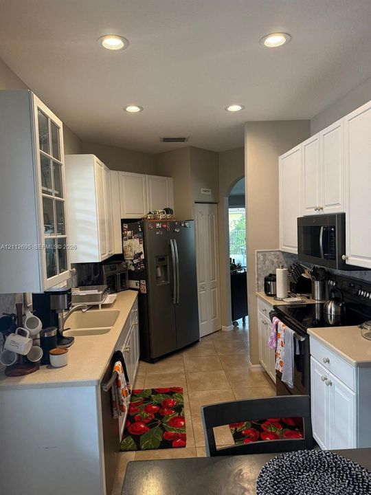 Kitchen featuring white shaker-style cabinetry, solid-surface countertops, recessed lighting, tile flooring, and glass-front upper cabinet doors