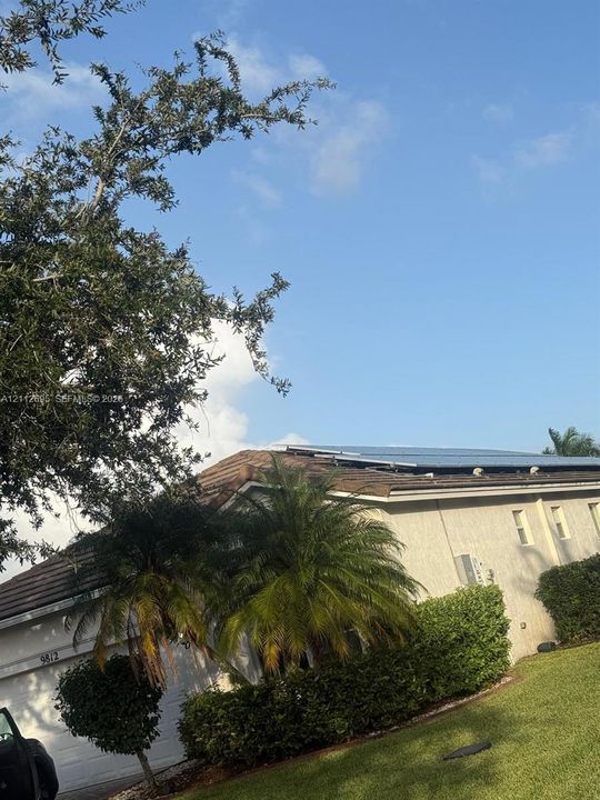 Exterior featuring a tiled roof with integrated solar panels, stucco siding, and mature landscaping