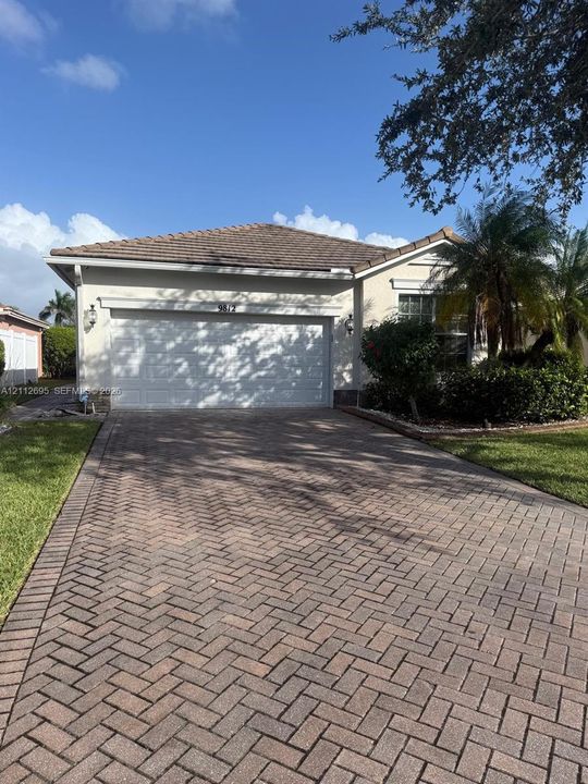 Stucco exterior featuring a tiled roof, herringbone-patterned paver driveway, two-car garage, and wall-mounted coach lighting