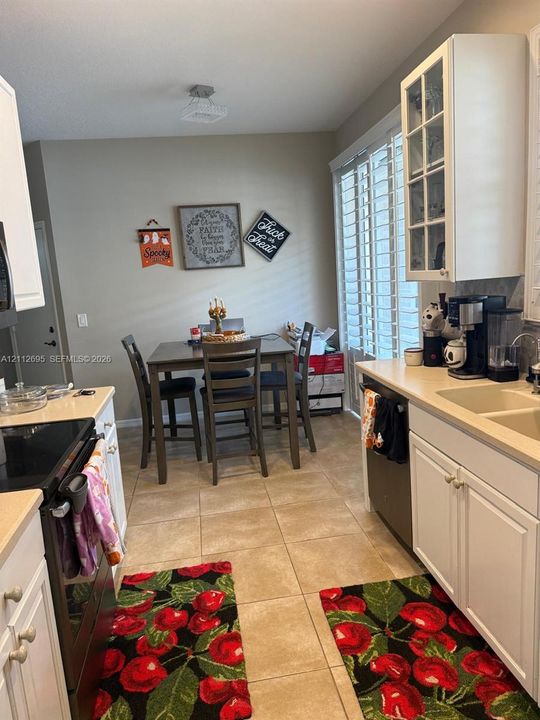 Kitchen featuring white shaker-style cabinetry, a glass-front upper cabinet, solid surface countertops, dual-basin sink, and ceramic tile flooring