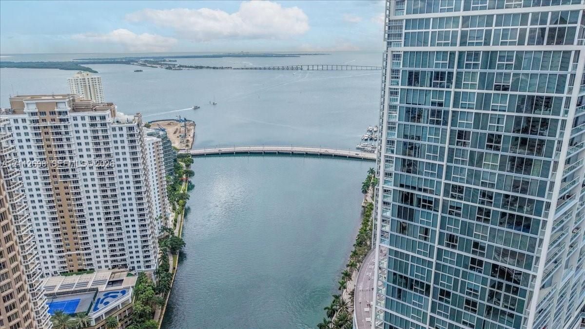 High-rise residential exterior with glass window grid, water expanse, bridge, and coastal horizon