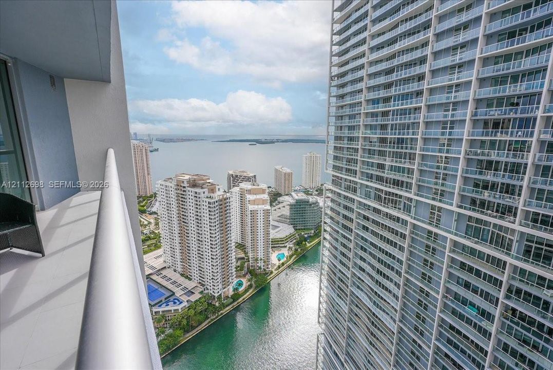 Covered balcony featuring glass and metal railings, overlooking urban high-rise buildings, a waterway, and a bay