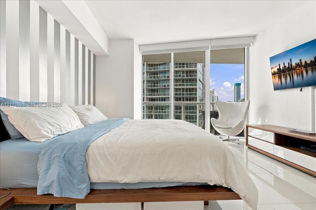 Floor-to-ceiling glass windows, wall-mounted television, vertical-paneled accent wall, and polished white tile flooring
