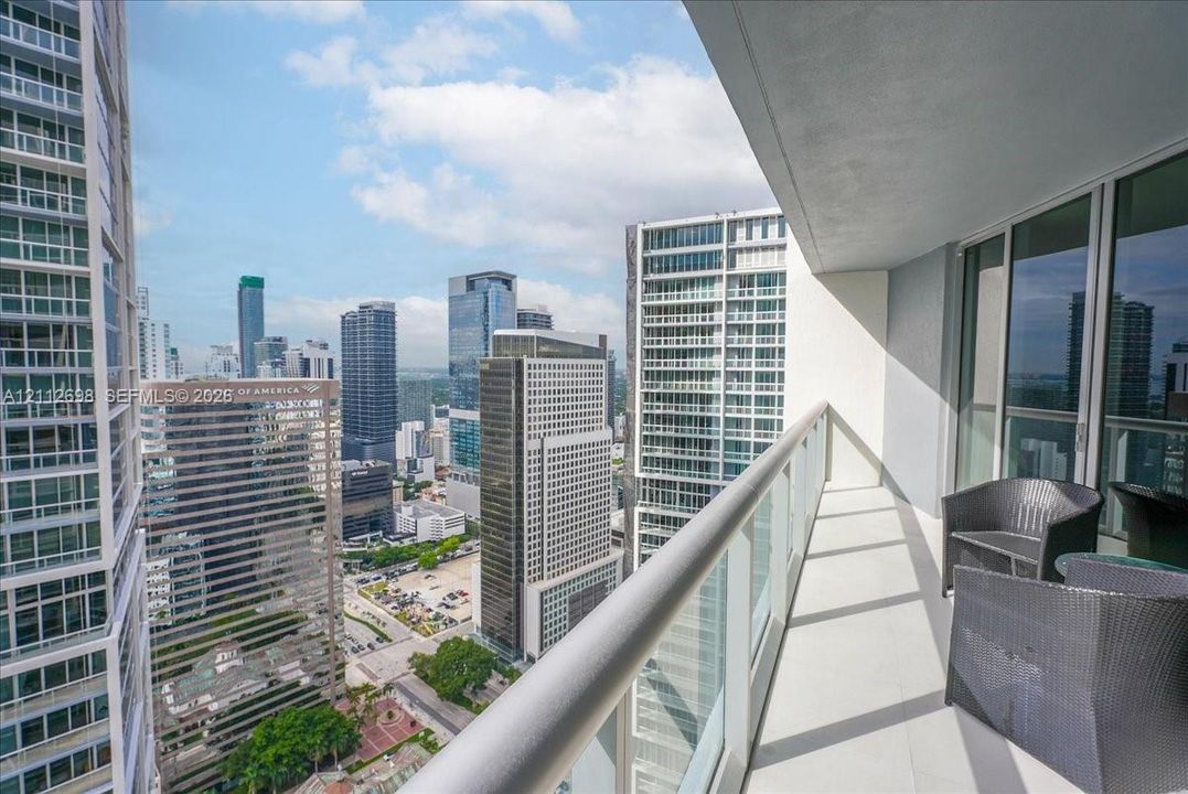Covered balcony featuring a metal railing with glass panels, concrete flooring, and urban high-rise surroundings