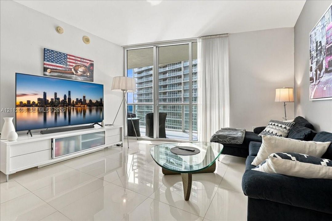 Living area featuring high-gloss tile flooring, floor-to-ceiling glass sliding doors, and a private balcony