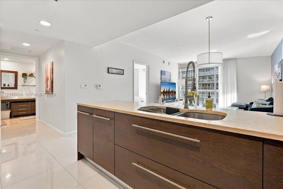 Kitchen island featuring dark wood-finish cabinetry, solid surface countertops, an undermount stainless steel double-basin sink, and a high-arc gooseneck faucet