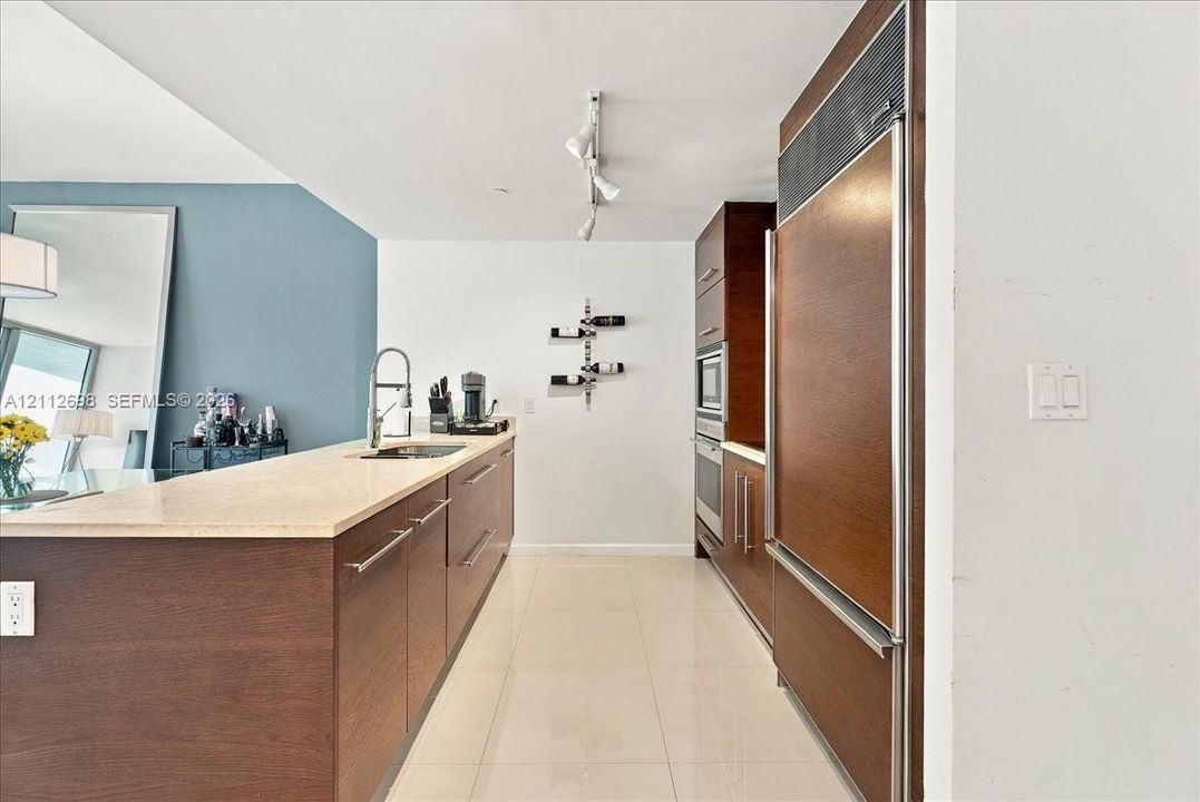 Kitchen featuring custom wood-finish cabinetry, stone countertop, integrated refrigerator, built-in wall oven and microwave, and polished tile flooring