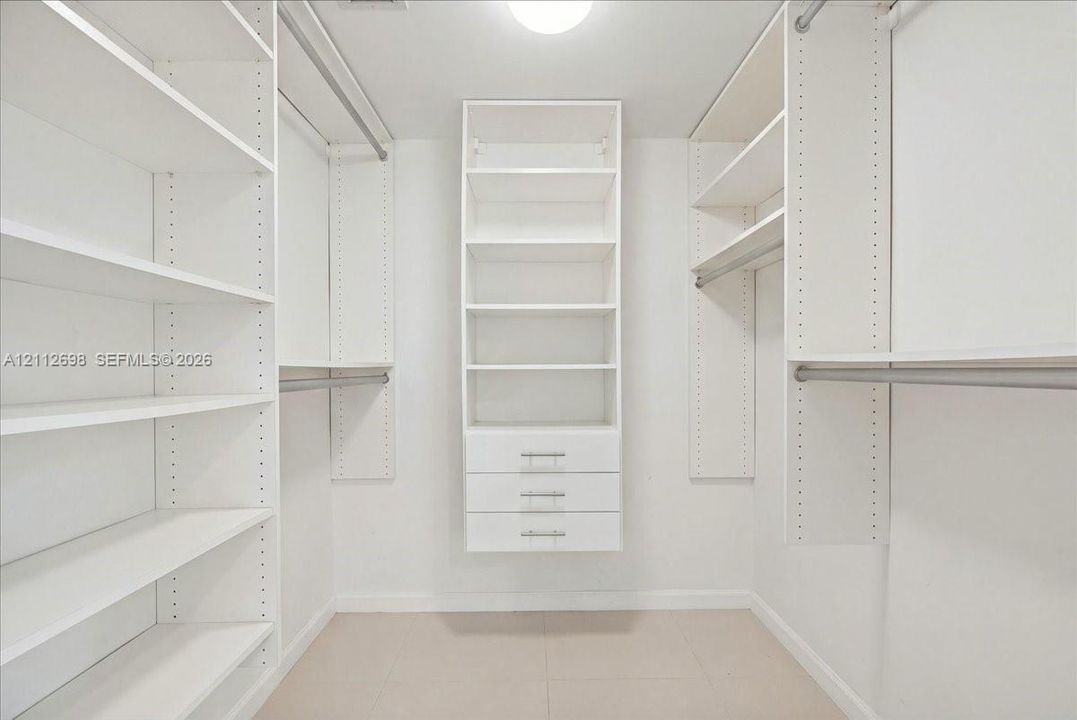 Walk-in closet featuring white built-in shelving, triple-drawer storage unit, metal hanging rods, and tile flooring