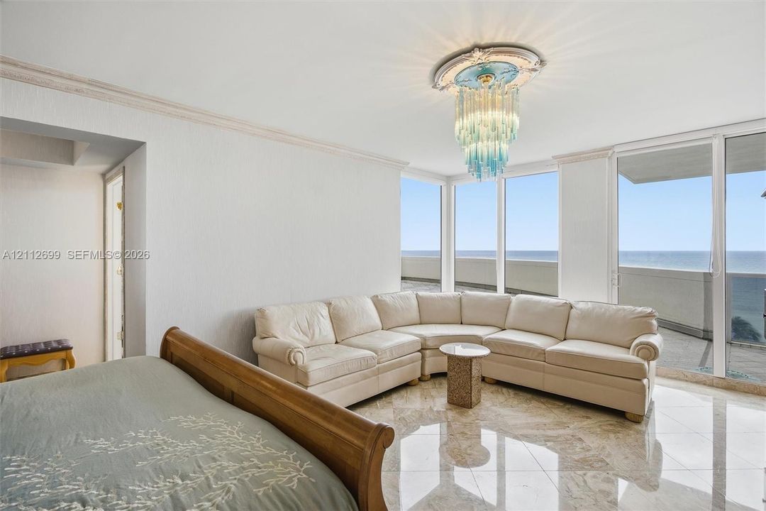 Floor-to-ceiling windows, polished stone flooring, intricate crown molding, and decorative ceiling medallion with a tiered glass chandelier