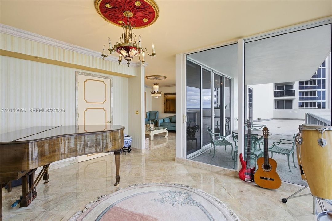 Polished stone flooring, intricate ceiling medallions with ornate light fixtures, and wall-to-wall sliding glass doors opening to an expansive balcony