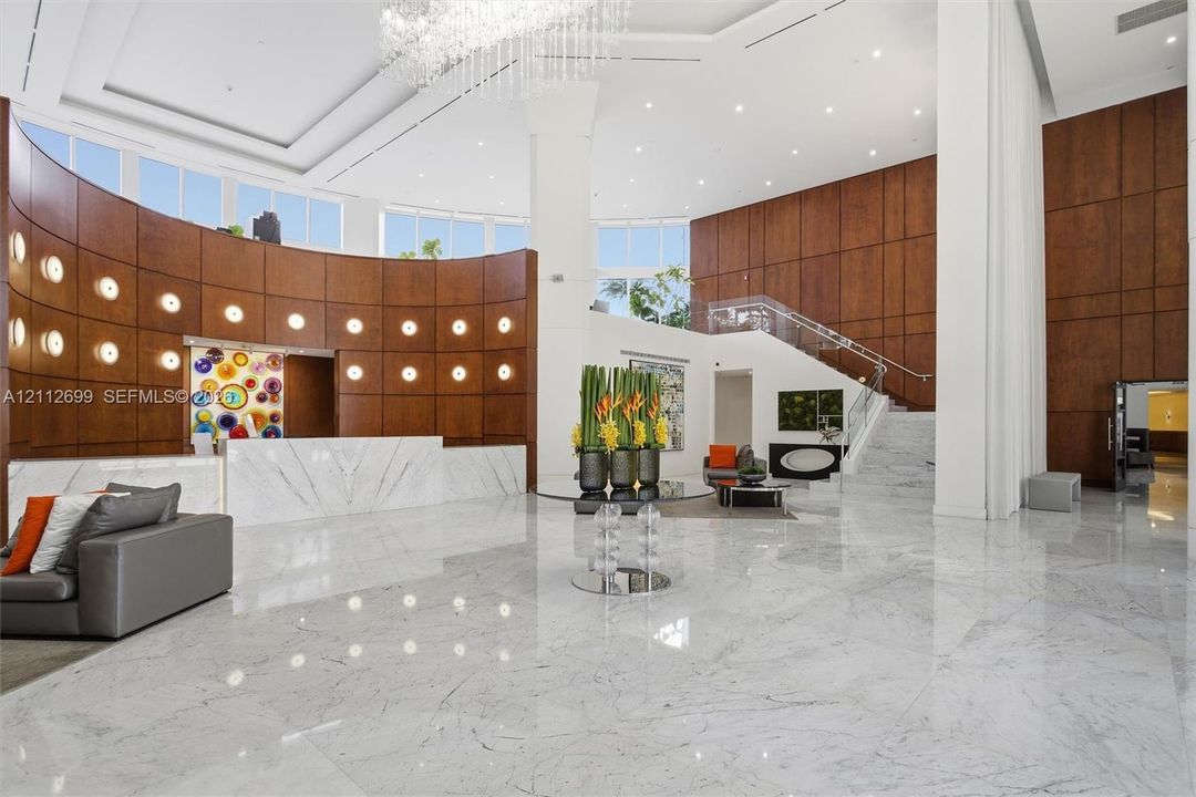 Grand entrance featuring high ceilings, polished stone flooring, curved wood-paneled walls, a statement crystal chandelier, and a built-in stone reception desk