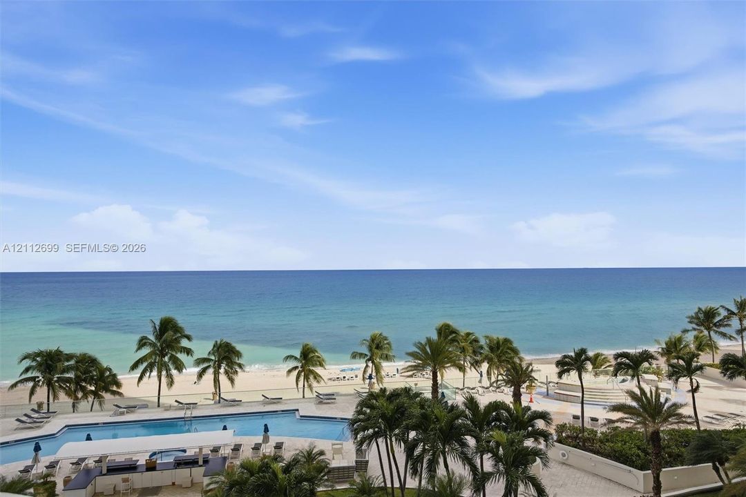 Oceanfront property featuring a swimming pool, paved pool deck, and landscaped palm trees