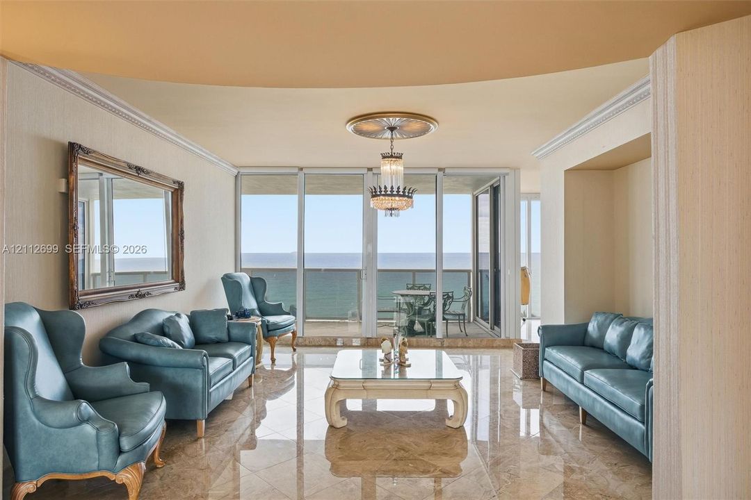 Polished stone flooring, expansive floor-to-ceiling glass panel doors, crown molding, and a crystal chandelier