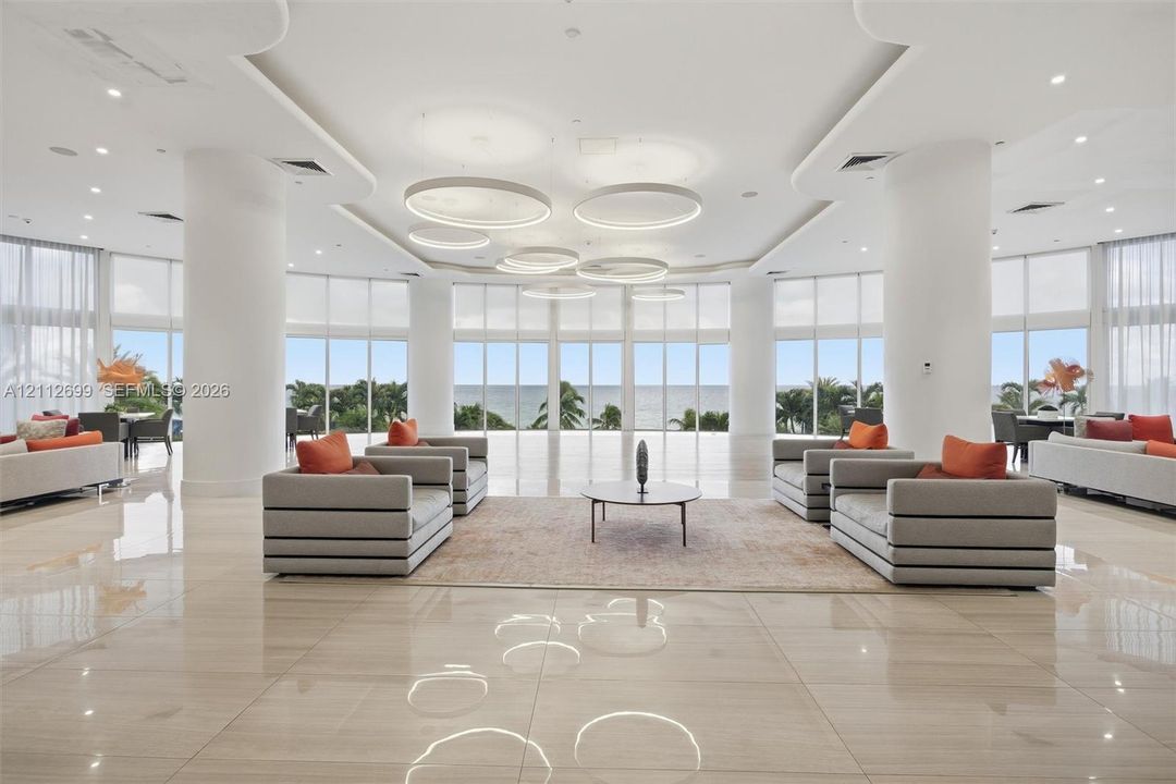 Expansive open-concept space featuring polished stone flooring, floor-to-ceiling windows, sculptural circular pendant lighting, recessed tray ceiling details, and structural support columns