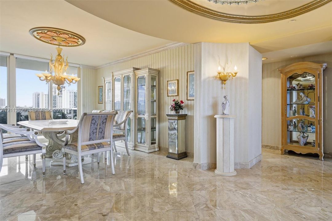 Polished stone flooring, custom architectural ceiling molding, decorative ceiling medallion, built-in cabinetry, and wall-mounted sconces