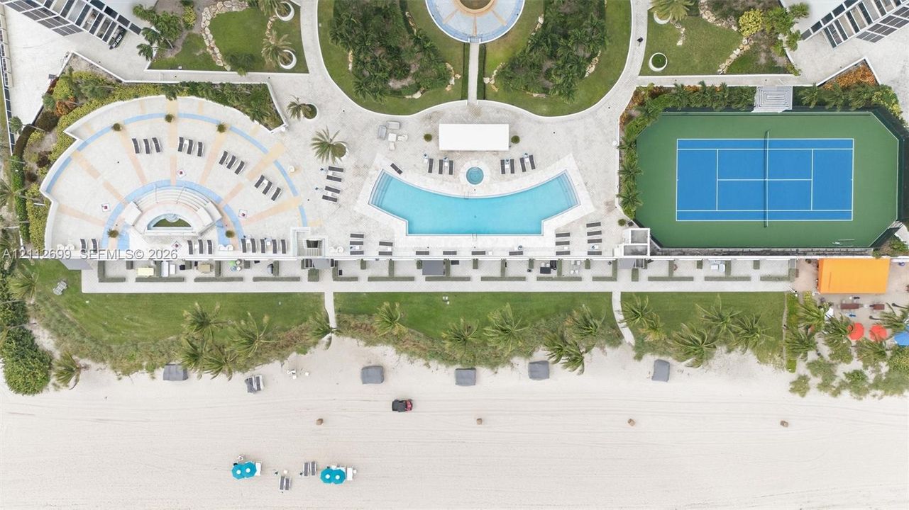 Oceanfront grounds featuring a swimming pool, hard-court tennis court, landscaped gardens, and paved recreation terrace