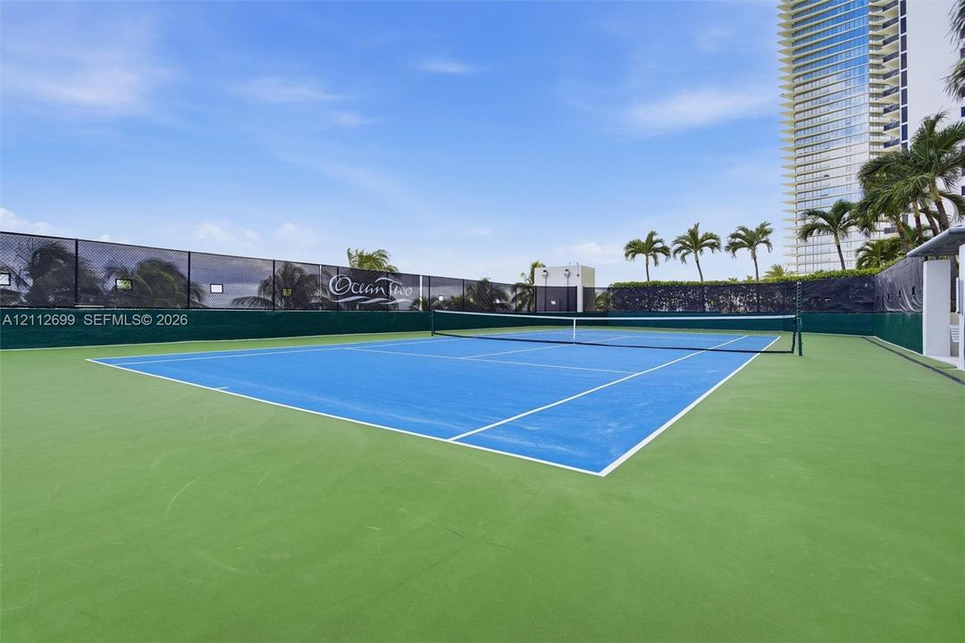 Tennis court with a dual-toned hard surface, perimeter privacy screening, and professional-grade netting