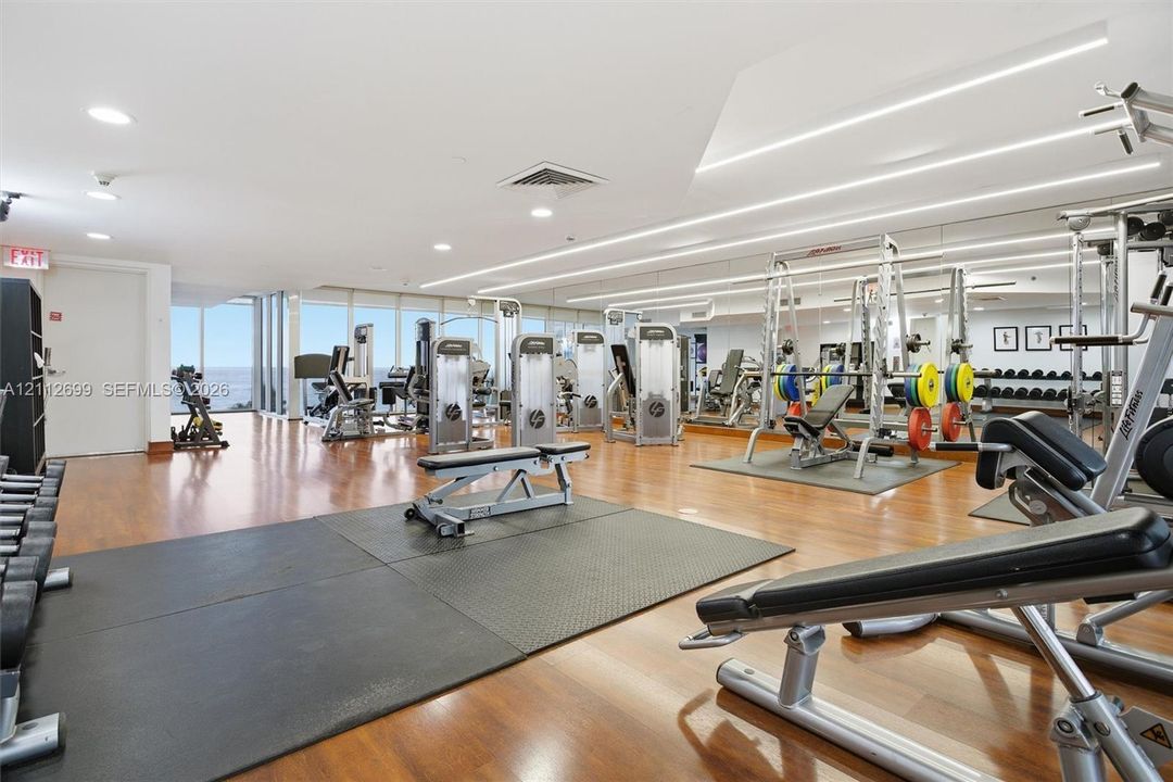 Fitness center featuring wood-finish flooring, full-wall mirrors, recessed lighting, and expansive floor-to-ceiling windows