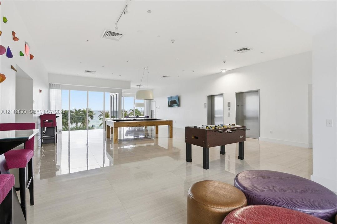 Open-concept common area featuring high-gloss tile flooring, floor-to-ceiling glass wall, recessed track lighting, and dual elevator access
