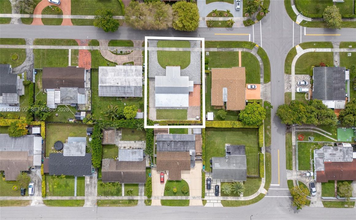 Aerial perspective of a property featuring a rectangular lot, a circular paved driveway, front and rear grass lawns, and established perimeter hedges