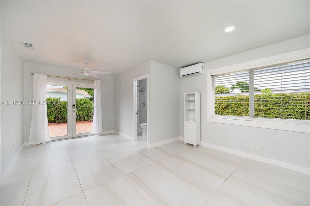 Large-format tile flooring, recessed lighting, ceiling fan, wall-mounted ductless climate control unit, and glass-paned double doors