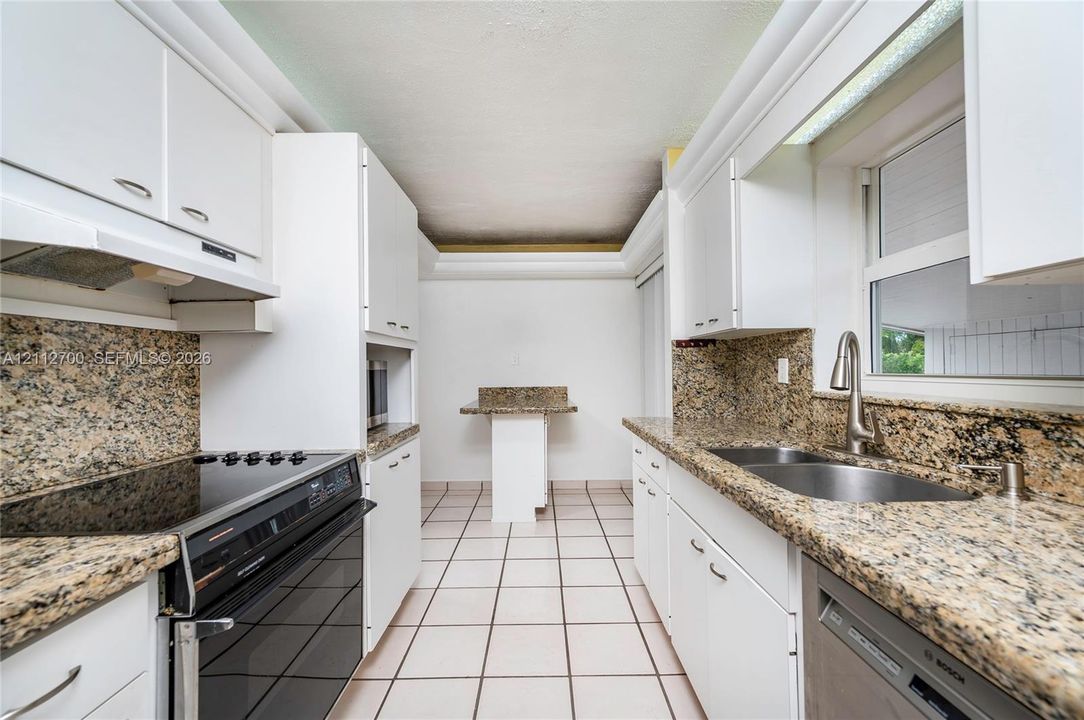 Kitchen featuring stone-finish countertops, tile flooring, white cabinetry, a dual-basin undermount sink, and built-in appliances