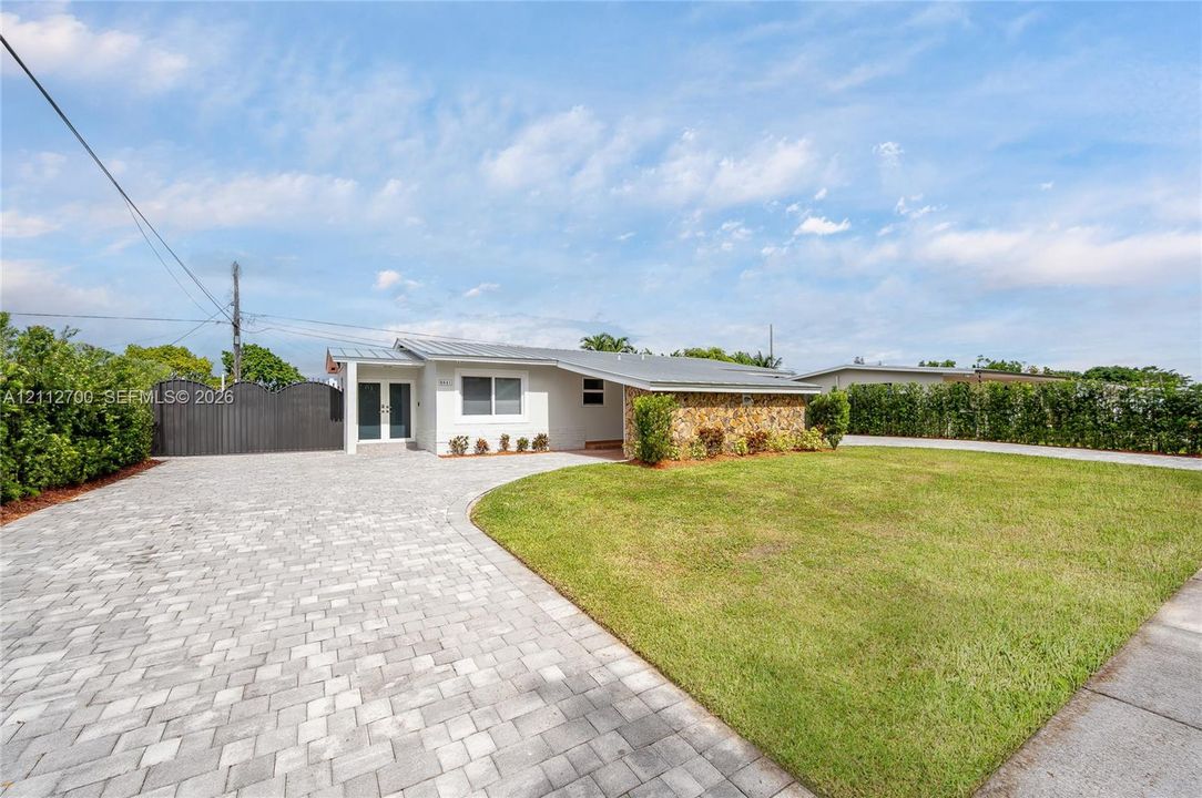 Single-story exterior featuring a stone-clad facade, metal roofing, expansive brick-paver driveway, and fenced perimeter