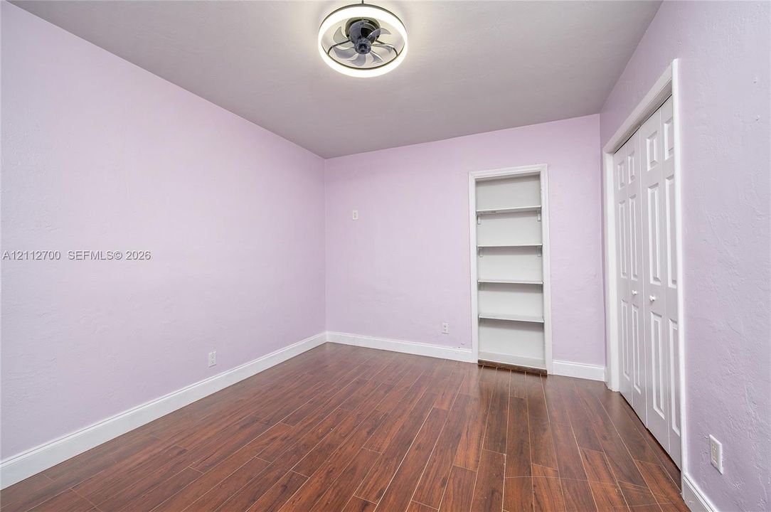 Interior space featuring wood-finish flooring, a built-in recessed wall shelving unit, double-door closet, and modern circular ceiling fan with integrated lighting