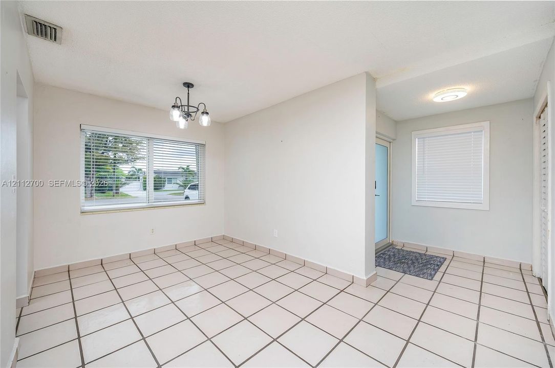 Ceramic tile flooring, multi-light hanging chandelier, and dual windows with integrated horizontal blinds