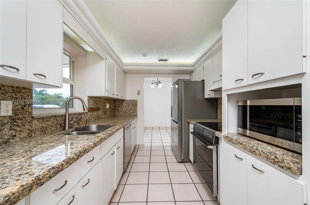 Kitchen featuring stone-finish countertops, white shaker-style cabinetry, stainless steel appliances, tile flooring, and a double-basin stainless steel sink with a high-arch faucet